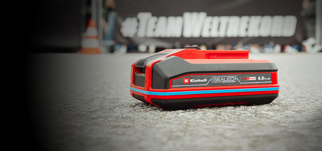 Einhell SEALED battery Power X-Change 4.0 Ah lies on asphalt, with the Guinness World Records "Record Holder" logo on the right.