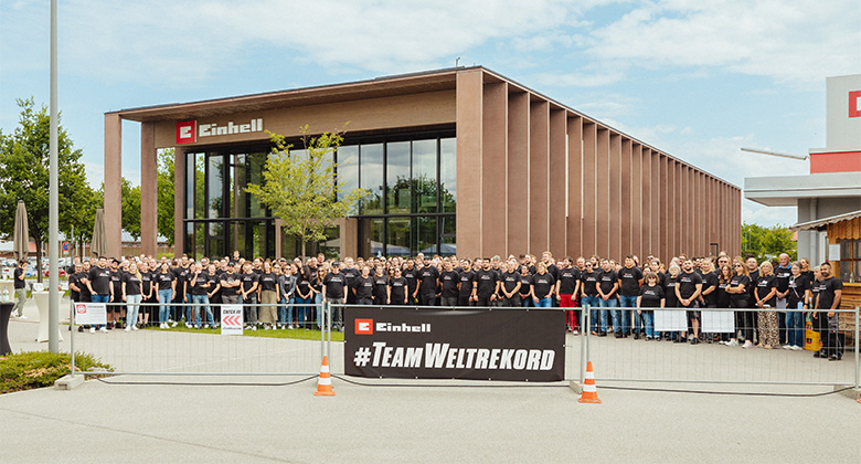 A large group of Einhell employees in black t-shirts posing behind a banner reading "#TeamWeltrekord".